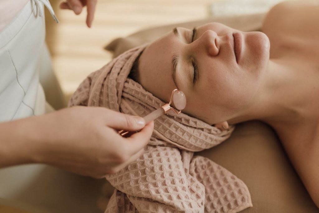 a-person-using-a-facial-roller-on-a-womans-face-6663465 A woman with closed eyes enjoying a peaceful facial roller treatment in a spa setting.
