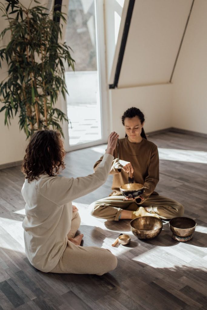 women-sitting-on-floor-doing-meditation-and-relaxation-with-tibetan-singing-bowls-and-tingsha-bells-6997995 Two women practicing meditation with Tibetan singing bowls in a serene indoor setting.